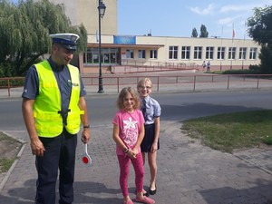 policjant z dziewczynkami na tle szkoły podstawowej