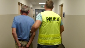 Policjant prowadzi korytarzem zatrzymanego oszusta