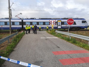 policjanci prowadzą oględziny na przejeździe kolejowym przy stojącym pociągu