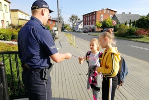 Policjant wręcza opaski odblaskowe dziewczynkom