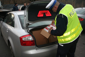 Policjant wyciąga z bagażnika zabezpieczone nielegalne papierosy