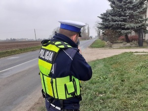 Policjant stoi na poboczu w miernikiem prędkości w dłoni