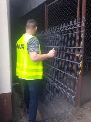 Policjant przestawia zabezpieczone metalowe ogrodzenie