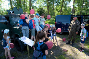 dzieci siedzą na masce wojskowego wozu bojowego a obok stoi żołnierz