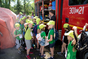 strażak pokazuje zgromadzonym dzieciom jakie mają wyposażenie w wozie strażackim