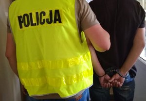 Zdjęcie założonych kajdanek na rękach zatrzymanego podczas prowadzenia go przez policjanta.