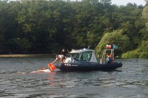 Policjanci wciągają na łódź osobę potrzebującą pomocy.